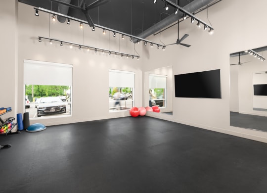 A yoga studio in a fitness center with weights, yoga balls, a TV, and windows.