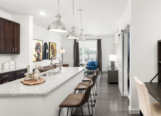 A kitchen with a spacious island with three barstools, next to a living room at Madamore Apartments.