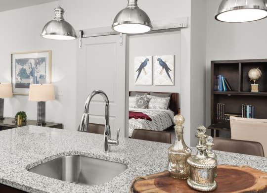 A kitchen island with a sink and granite countertops, and light fixtures.