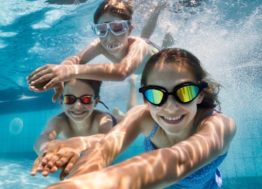 Three people wearing goggles are swimming underwater.