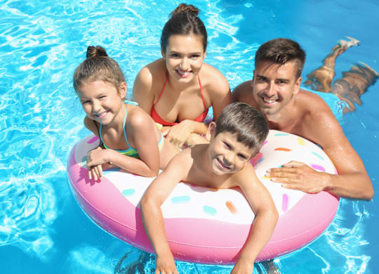 Four people are floating on a pink inflatable in a blue pool.
