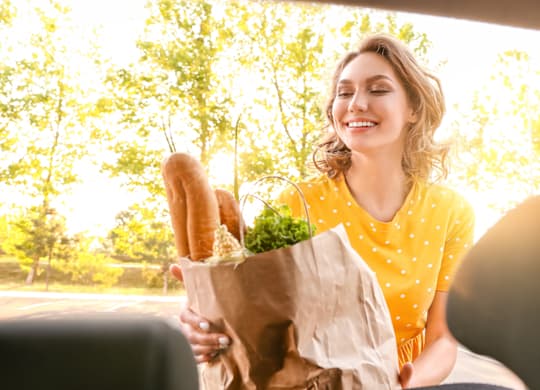 A woman in a yellow dress is holding a paper bag with groceries in it.