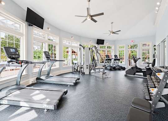 A fitness center equipped with cardio machines and weights surrounded by windows at Reserve at Hamburg.