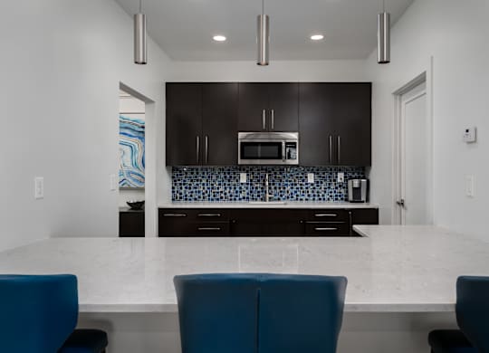 Contemporary kitchen with large island, white countertops, and blue bar stools at The Coleman Apartments