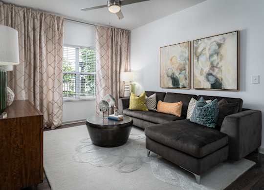 Spacious living room with brown leather couch, round coffee table, ceiling fan, and natural light at The Coleman in Canal Winchester, OH