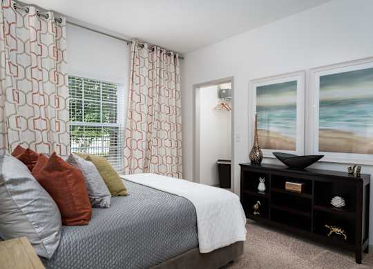 Furnished bedroom with plush carpeting, large bed, dresser, window, and modern decor at The Coleman in Canal Winchester, OH
