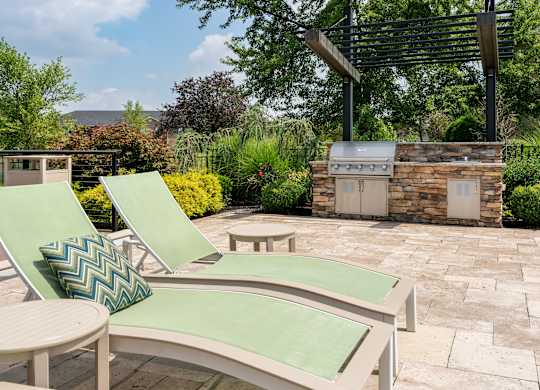 Outdoor patio with grill and two lounge chairs, perfect for relaxing at The Coleman