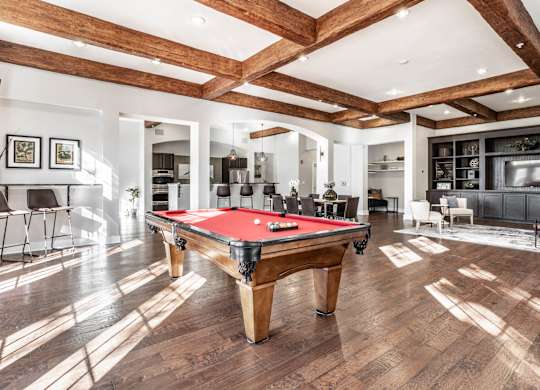A pool table is in the middle of a room with wooden floors and a high ceiling.