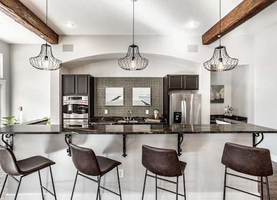 A modern kitchen with a black countertop and brown chairs.