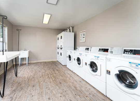 A laundry room with a slection of white washers and dryers on hardwood-style flooring at The Oaks.