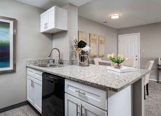 A kitchen equipped with white cabinets, granite countertops, and black appliances, next to a dining room table.