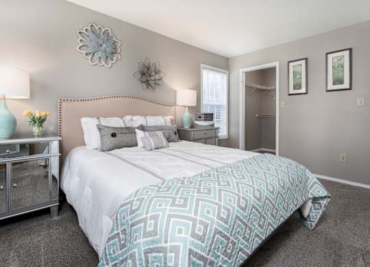 A furnished bedroom with a closet, carpeted flooring, a window, and decor.