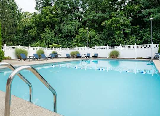 A swimming pool in Reynoldsburg, OH surrounded by blue chairs, a white fence, and large trees.