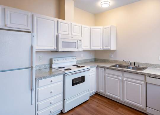 A white kitchen with a refrigerator, stove, oven, microwave, and cabinets.