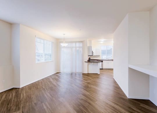 an empty living room with hard wood floors and a kitchen