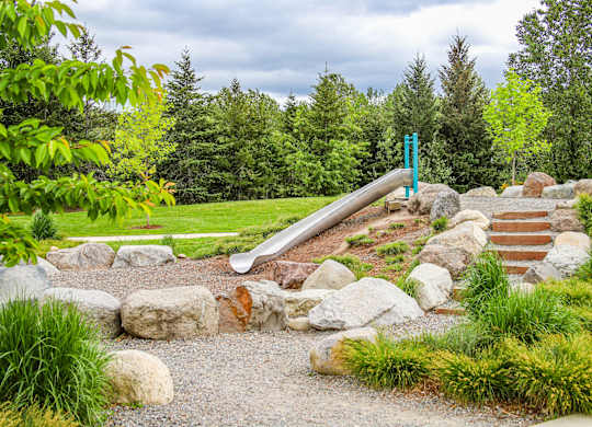 A playground with a green slide and rocks.