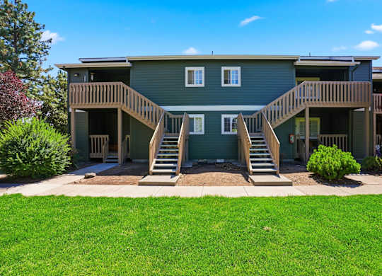 A green house with a wooden deck and stairs leading to the entrance.