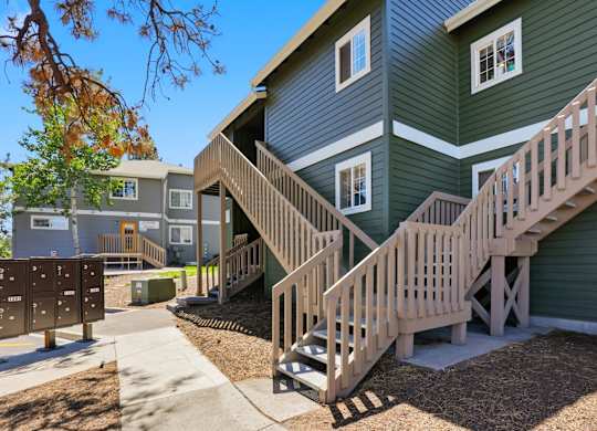 A green house with a wooden staircase leading to the second floor.