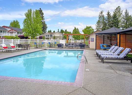 Outdoor Swimming Pool with Lounge Chairs, Shade Gazebos, and Lush Greenery at Clock Tower Village, Washington
