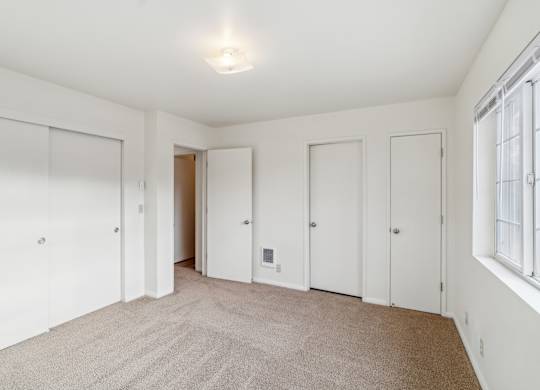 A white room with a carpeted floor and a window on the right side.