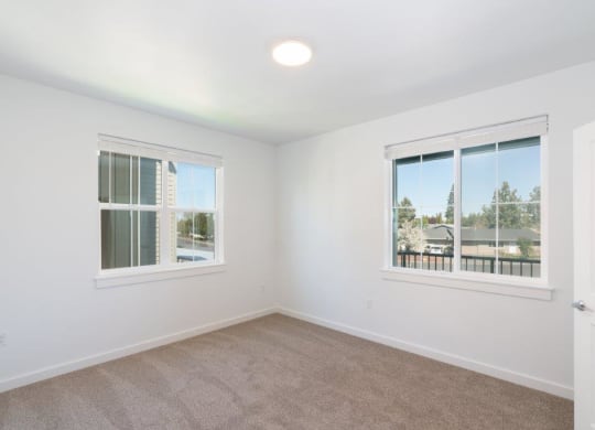 an empty bedroom with two windows and a door to a balcony