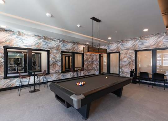 a pool table in a billiards room with windows and a bar
