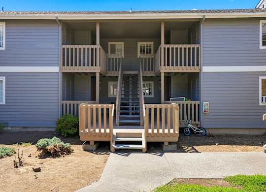 A two-story apartment building with a balcony and stairs leading to the second floor.