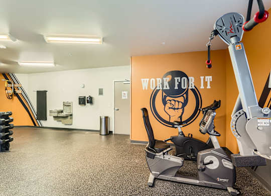 A gym with a row of treadmills and a wall with a fist graphic and the words "work for it".