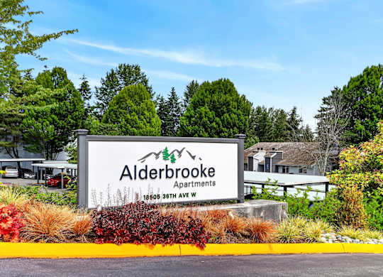 A sign for Alderbrooke Apartments is displayed in front of some trees.