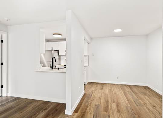 a living room and kitchen with white walls and wood floors