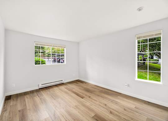 a living room with white walls and wood floors and a window