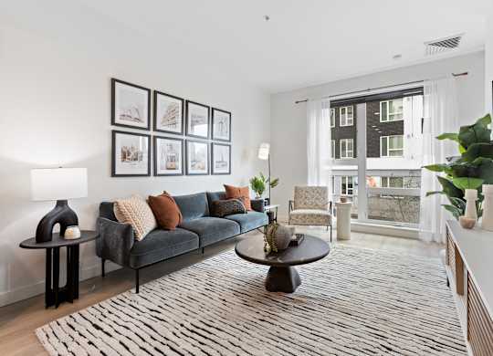 A living room with a grey couch, a coffee table, and a large window.