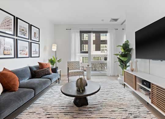 A living room with a grey couch, a black coffee table, and a large window with a view of a building outside.