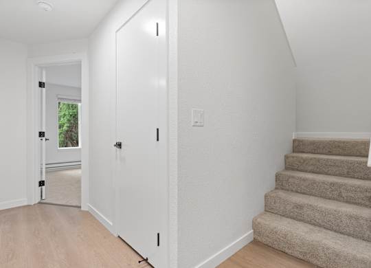 A hallway with a staircase and a door leading to a balcony.