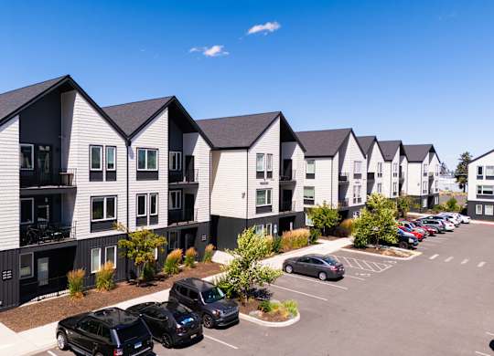 A row of modern townhouses with cars parked in the driveway.