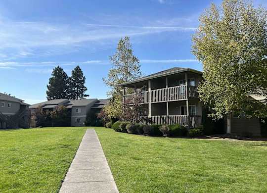 A walkway leads to a building with a tree on the left and another on the right.