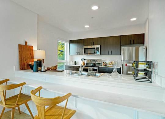 A modern kitchen with wooden chairs and white countertops.