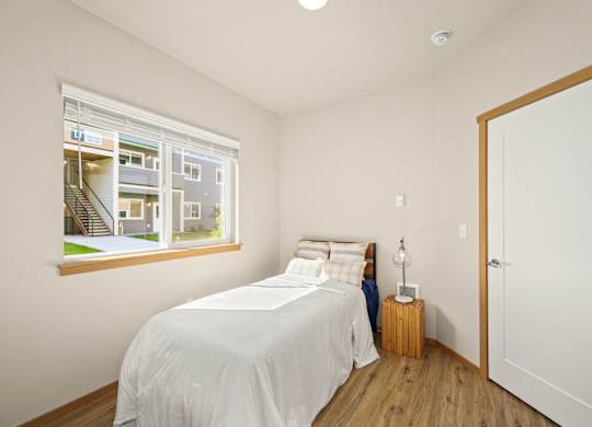 A bedroom with a large bed and a view of a building outside the window.