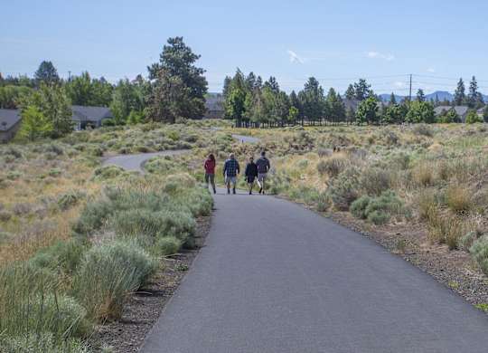 Three people walking on a paved trail through a grassy area.