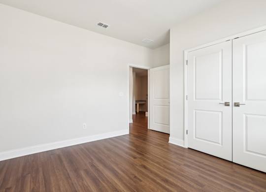 A room with white walls and wooden floors with a white door on the right.
