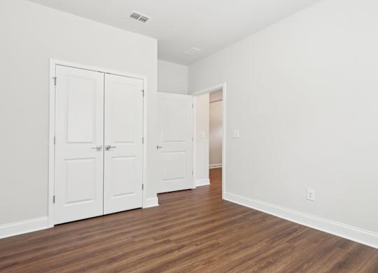 A room with white walls and wood flooring with three white doors.