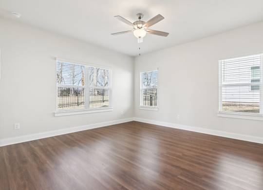 A room with a ceiling fan and two windows.