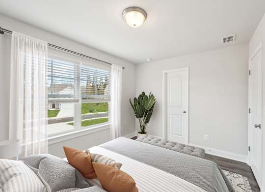 A bedroom with a large bed and a window with white curtains.