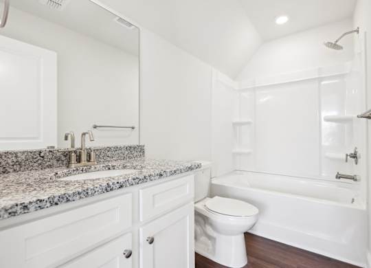 A white bathroom with a granite countertop and a white bathtub.