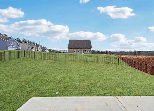 A large grassy field with a fence and a house in the background.