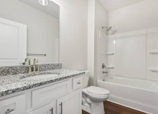 A white bathroom with a marble countertop and a white bathtub.