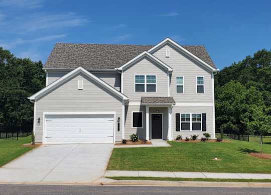 A two-story house with a garage is surrounded by a green lawn and trees.