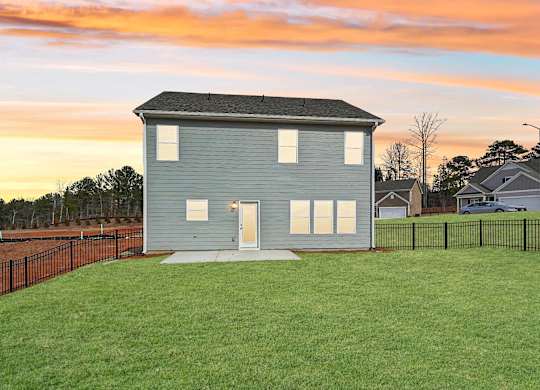 A house with a grey roof and white windows is surrounded by a black fence.