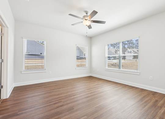 A room with a ceiling fan and two windows.
