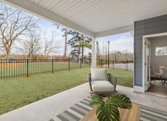 a patio with a chair and a table and a yard with a fence